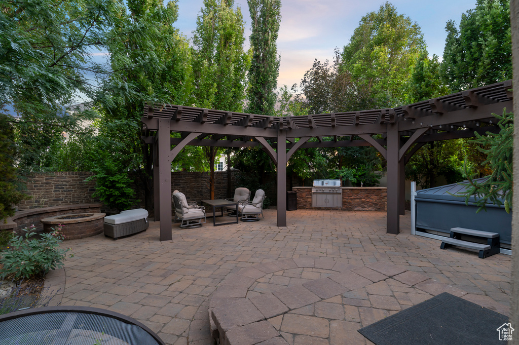 Patio terrace at dusk featuring exterior kitchen, a patio area, a pergola, and a jacuzzi