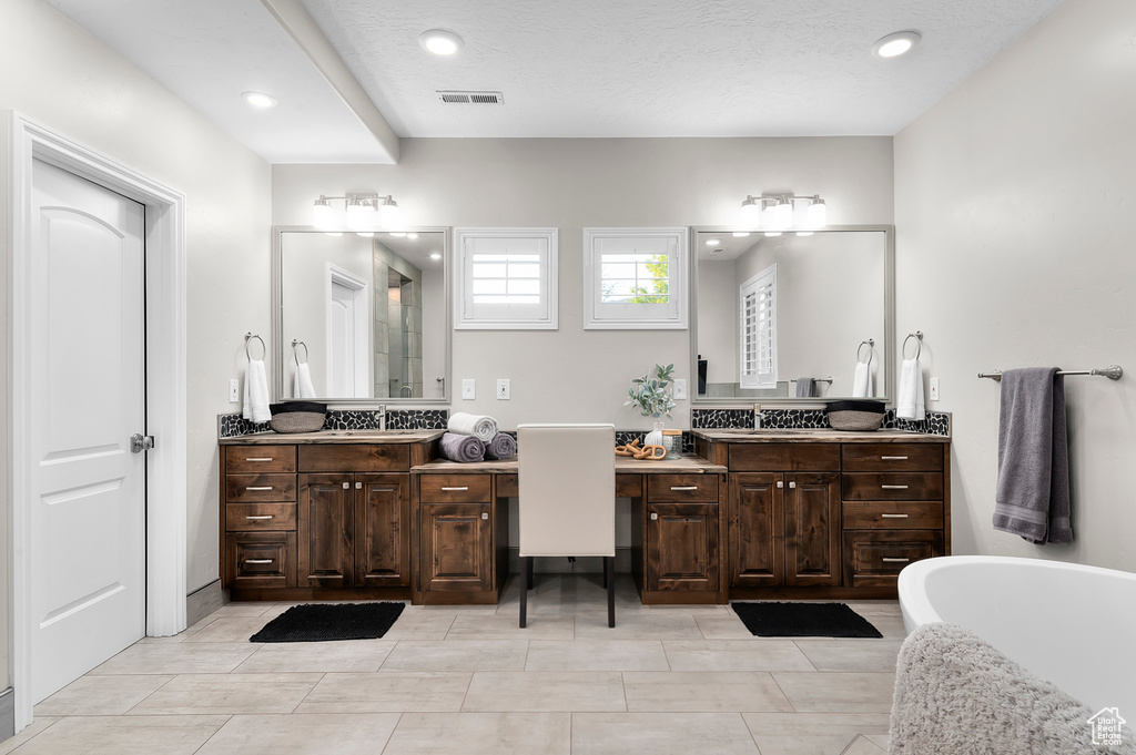 Full bath with two vanities, a freestanding tub, a shower with shower door, and recessed lighting