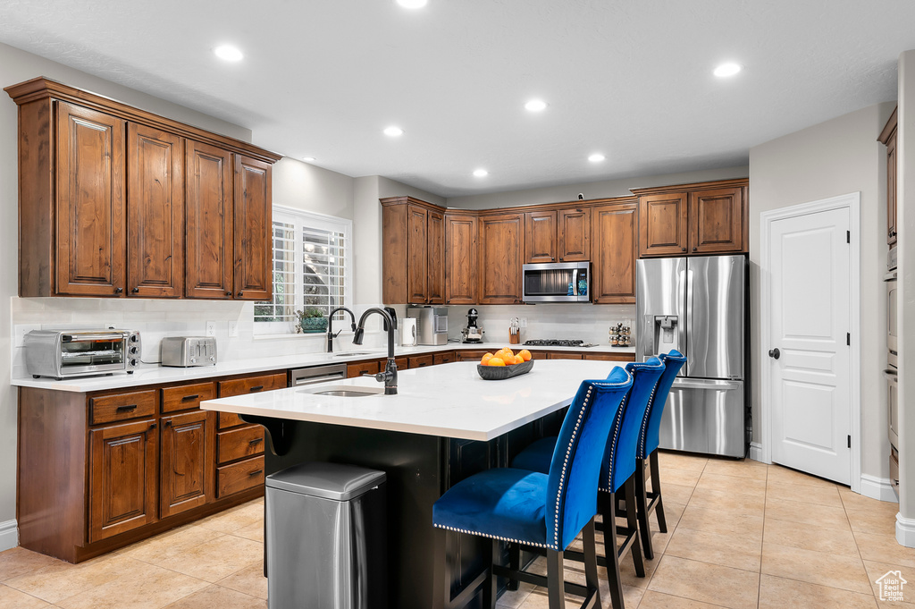 Kitchen featuring appliances with stainless steel finishes, decorative backsplash, light countertops, a center island with sink, and recessed lighting