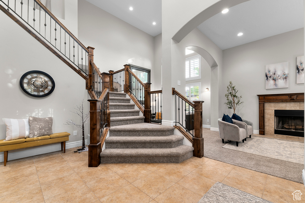 Staircase with arched walkways, a towering ceiling, recessed lighting, a premium fireplace, and tile patterned floors