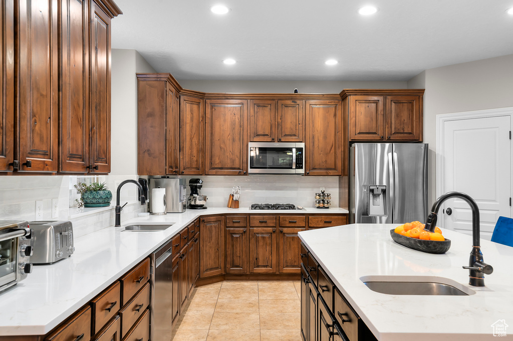 Kitchen with appliances with stainless steel finishes, recessed lighting, tasteful backsplash, light tile patterned floors, and light stone counters