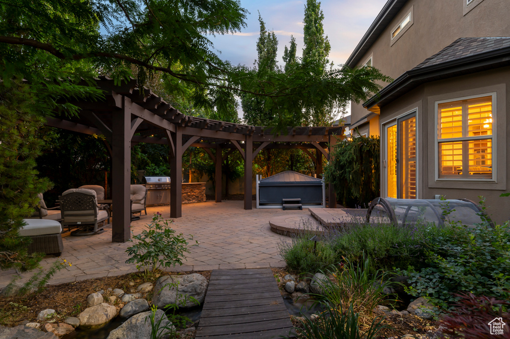 Deck at dusk featuring a patio area, a pergola, an outdoor kitchen, and a jacuzzi