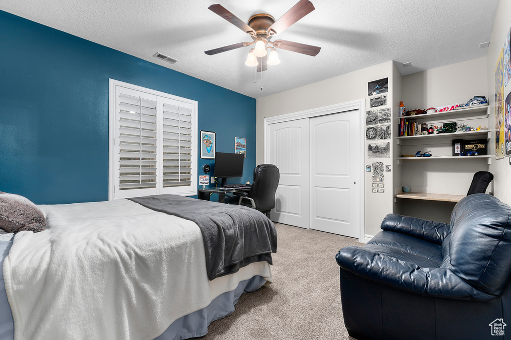 Carpeted bedroom with a closet, a desk, ceiling fan, and a textured ceiling