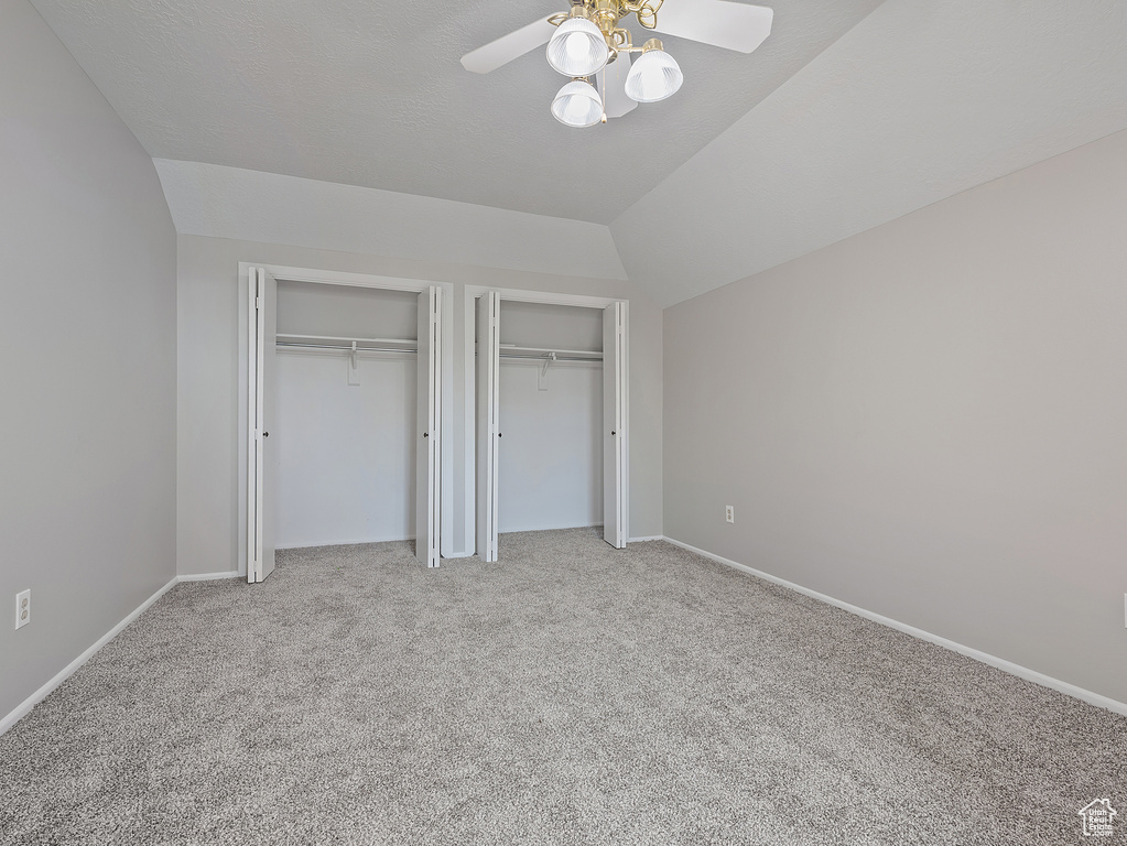 Unfurnished bedroom with two closets, light carpet, vaulted ceiling, and ceiling fan