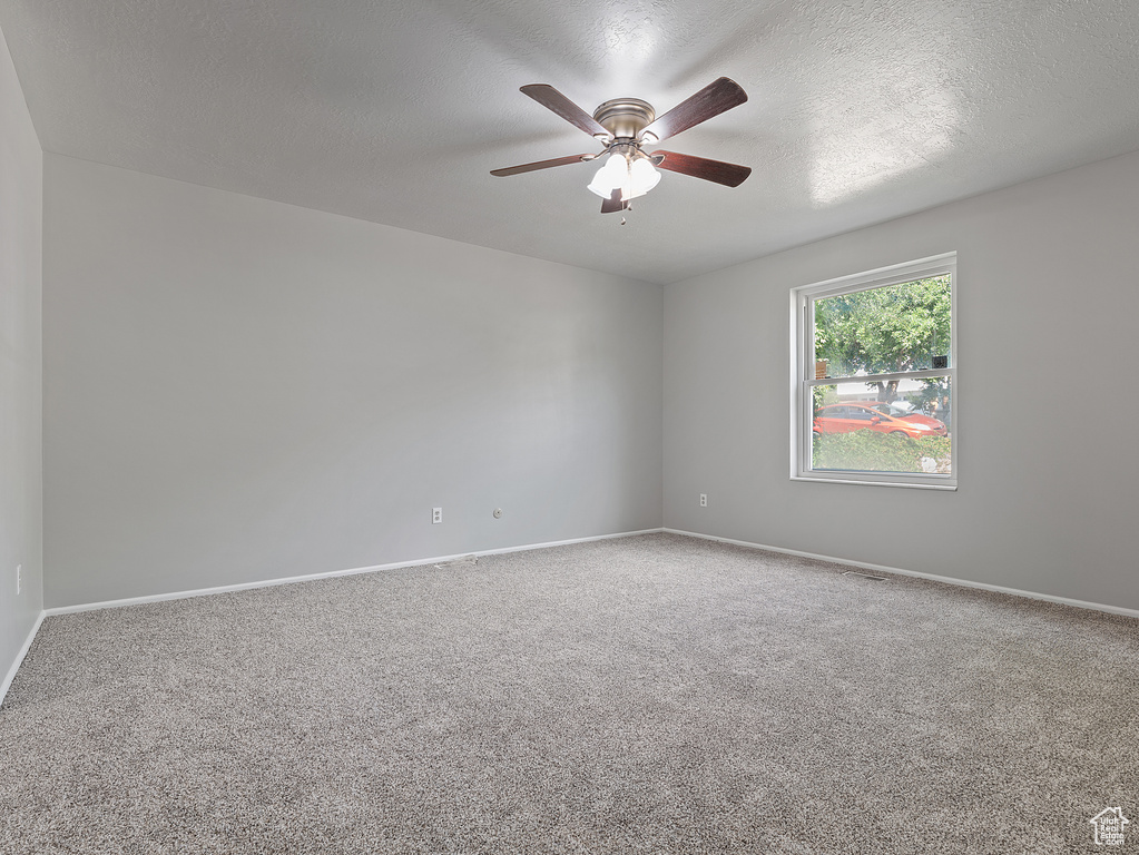 Empty room featuring carpet floors, a ceiling fan, and a textured ceiling