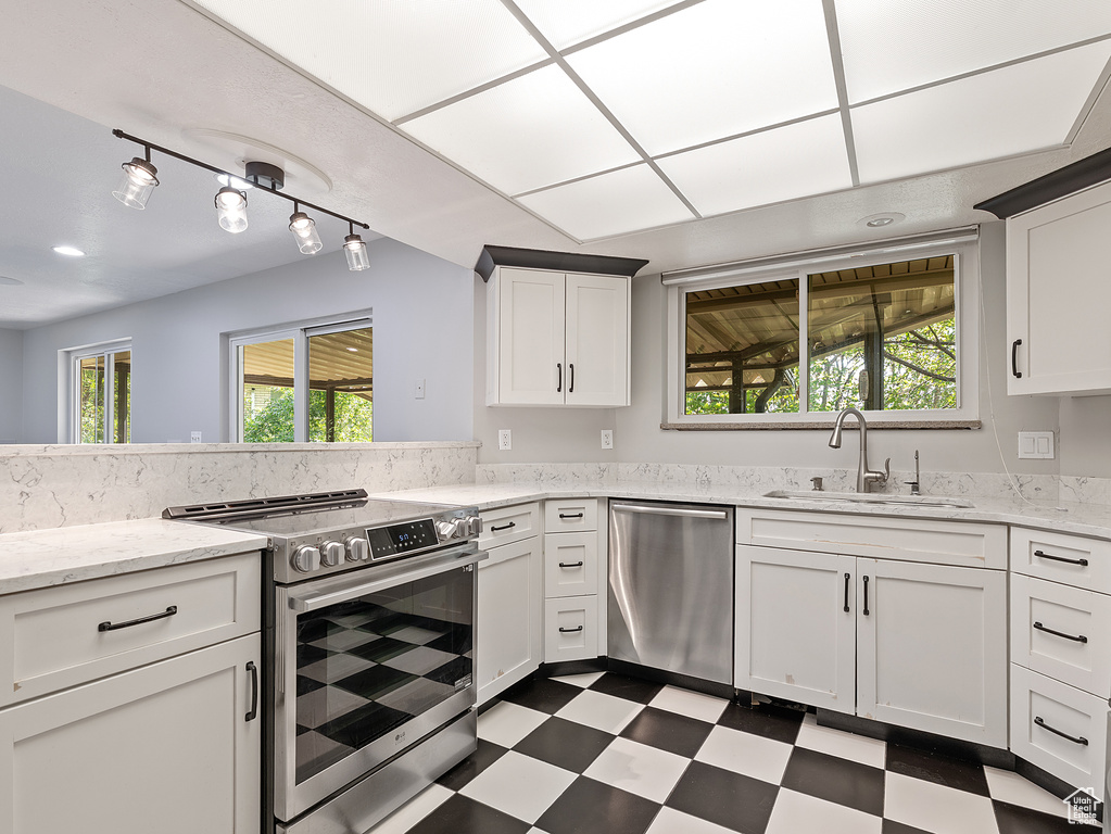 Kitchen featuring stainless steel appliances, dark flooring, white cabinets, and plenty of natural light