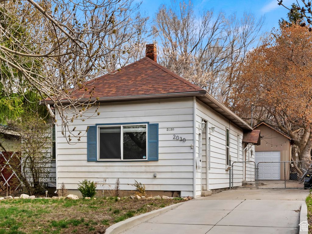 View of front of home featuring a chimney, a gate, a garage, driveway, and a shingled roof