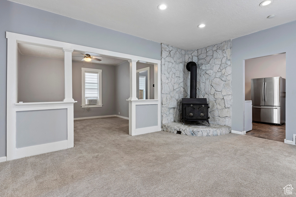 Unfurnished living room featuring carpet flooring, a wood stove, baseboards, ceiling fan, and recessed lighting