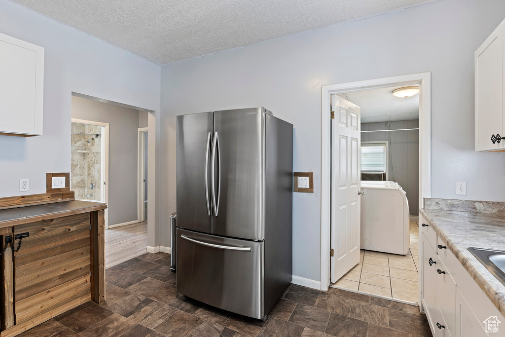 Kitchen featuring freestanding refrigerator, washer / dryer, white cabinetry, light countertops, and baseboards