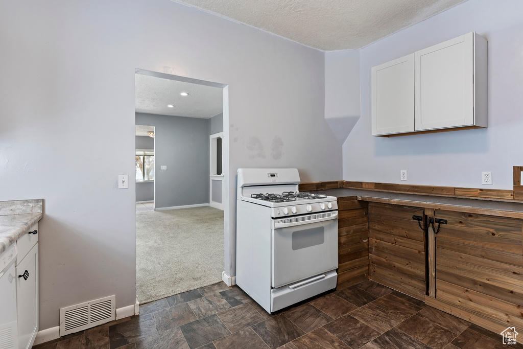 Kitchen featuring white appliances, white cabinets, light countertops, baseboards, and dark colored carpet