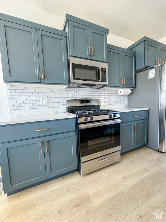 Kitchen featuring appliances with stainless steel finishes, light wood finished floors, tasteful backsplash, light countertops, and blue cabinets