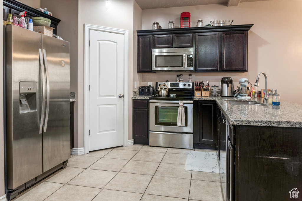 Kitchen featuring stainless steel appliances, light stone counters, a peninsula, light tile patterned flooring, and dark brown cabinetry