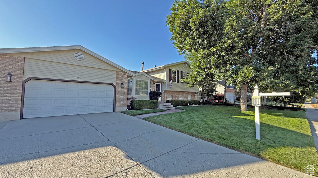 Tri-level home featuring brick siding, concrete driveway, a front lawn, and a garage