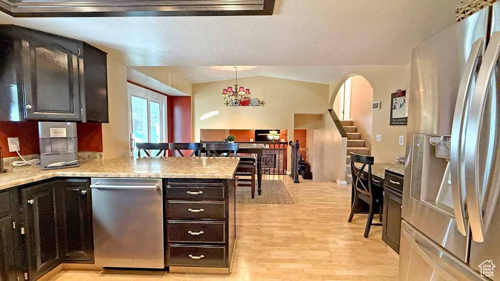 Kitchen featuring appliances with stainless steel finishes, light wood-style floors, a peninsula, light countertops, and decorative light fixtures