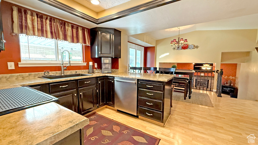Kitchen with stainless steel dishwasher, light countertops, a chandelier, light wood-style floors, and vaulted ceiling