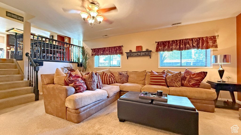 Living area featuring a ceiling fan, carpet, plenty of natural light, and stairs