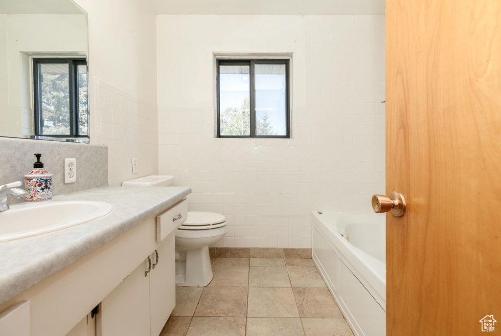Bathroom featuring tile walls, healthy amount of natural light, vanity, a tub to relax in, and tile patterned flooring