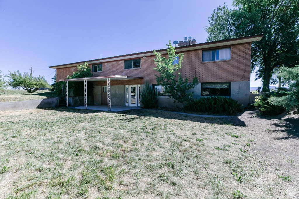 View of front of property with a patio, brick siding, a front yard, and an attached carport