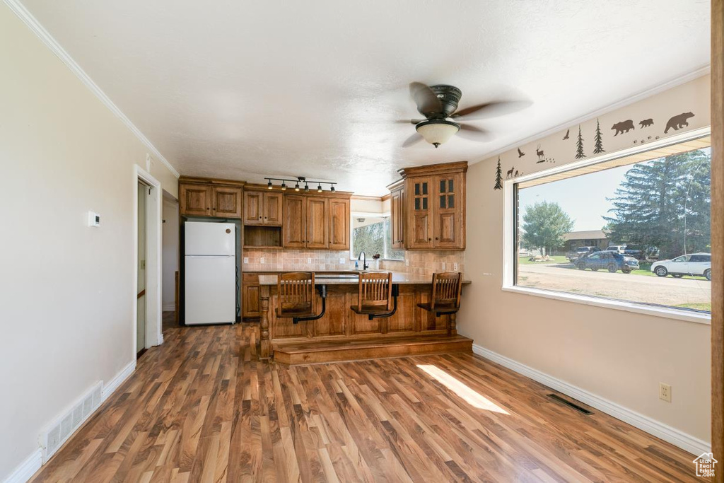 Kitchen with freestanding refrigerator, brown cabinets, a peninsula, tasteful backsplash, and wood finished floors