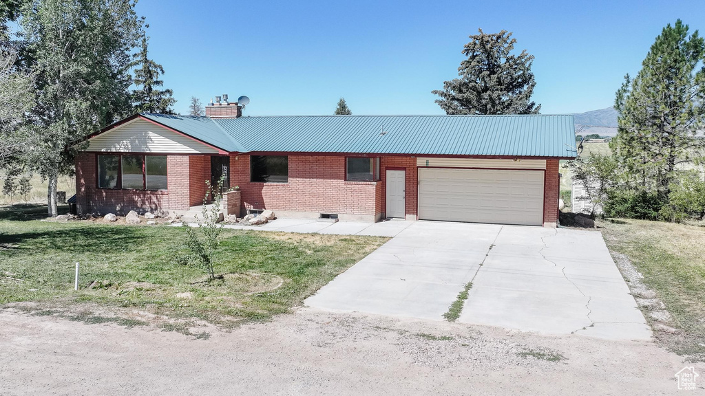 Ranch-style home featuring a garage, driveway, a front lawn, and a metal roof