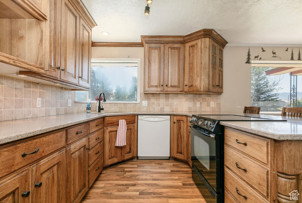 Kitchen with dishwasher, electric range, light wood-style floors, light stone counters, and brown cabinetry