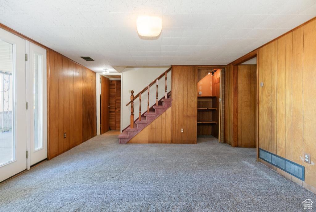Unfurnished living room featuring carpet, stairway, and wood walls