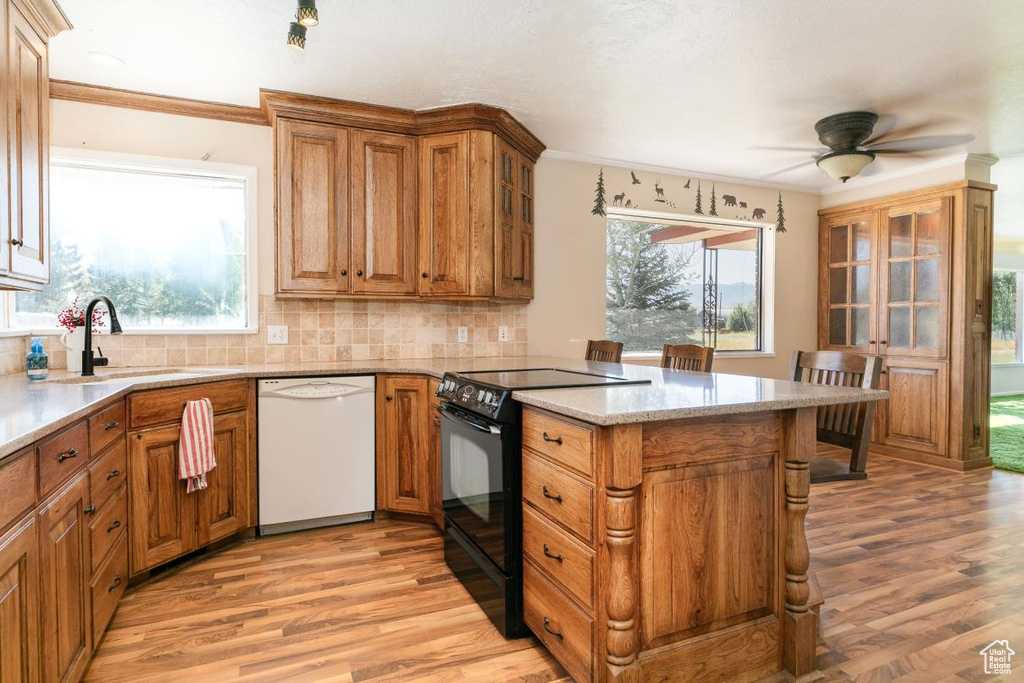 Kitchen with white dishwasher, black range with electric cooktop, a peninsula, light wood-style flooring, and ornamental molding