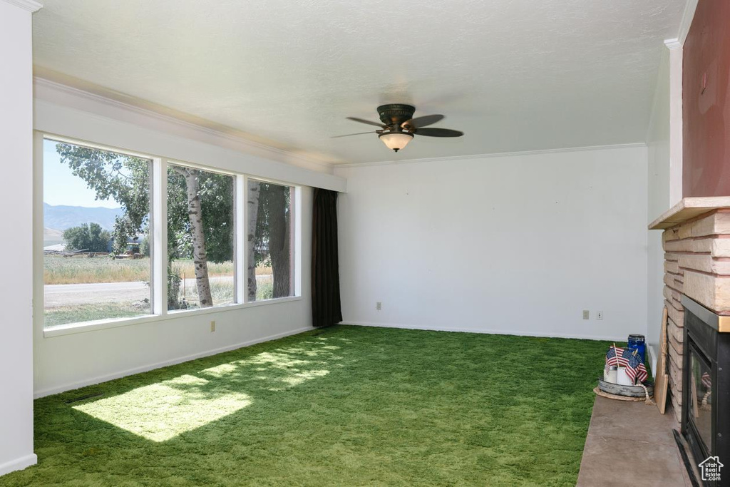 Unfurnished living room featuring a stone fireplace, carpet floors, ceiling fan, ornamental molding, and a mountain view
