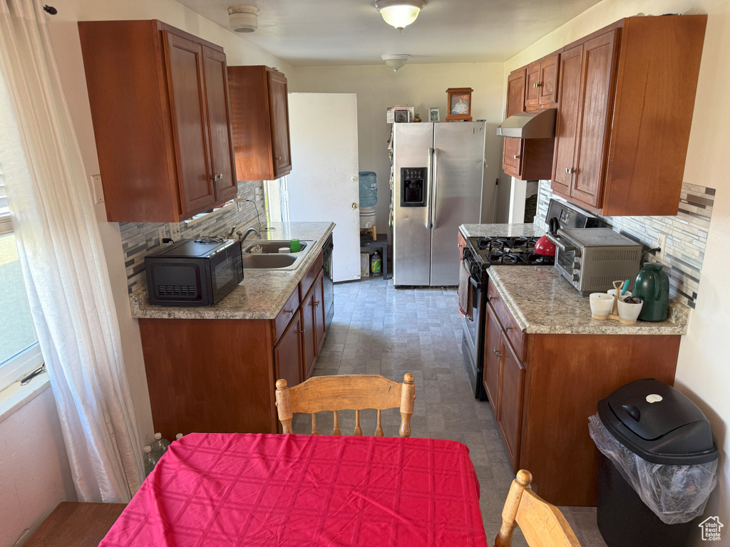 Kitchen with range with gas cooktop, ventilation hood, stainless steel fridge, black microwave, and decorative backsplash