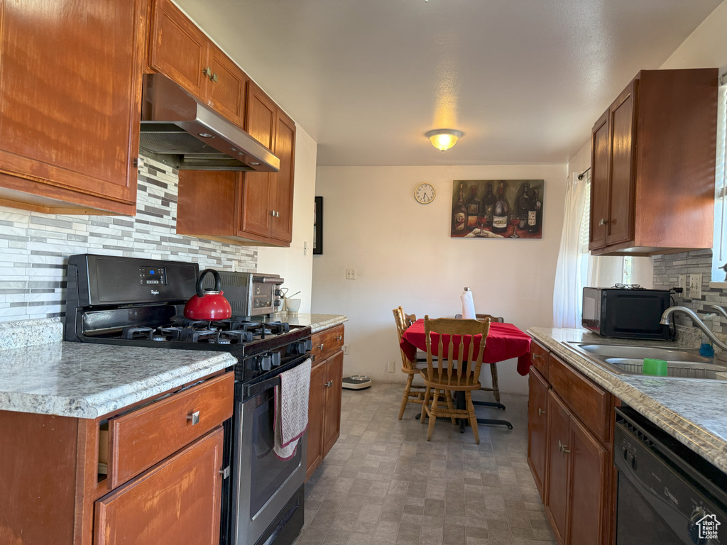 Kitchen with black appliances, under cabinet range hood, backsplash, light countertops, and brown cabinetry