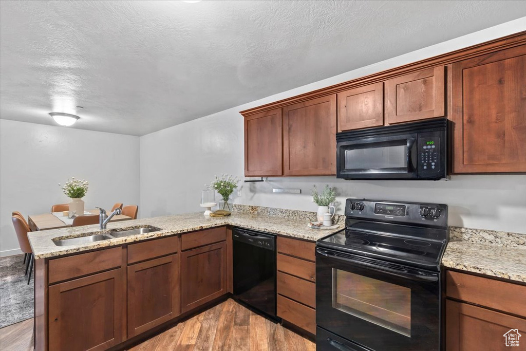 Kitchen with black appliances, a peninsula, light wood-style flooring, light stone counters, and a textured ceiling