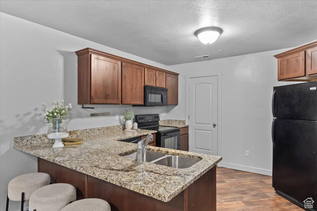Kitchen featuring black appliances, a peninsula, a kitchen breakfast bar, light stone countertops, and dark wood finished floors