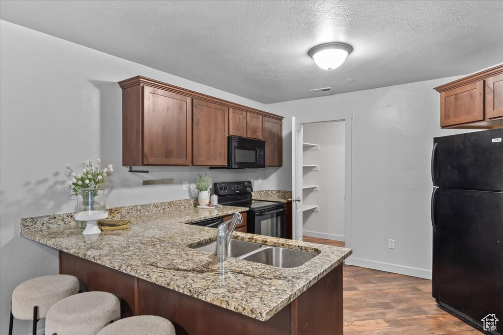 Kitchen featuring black appliances, a peninsula, a kitchen breakfast bar, light stone countertops, and dark wood-type flooring