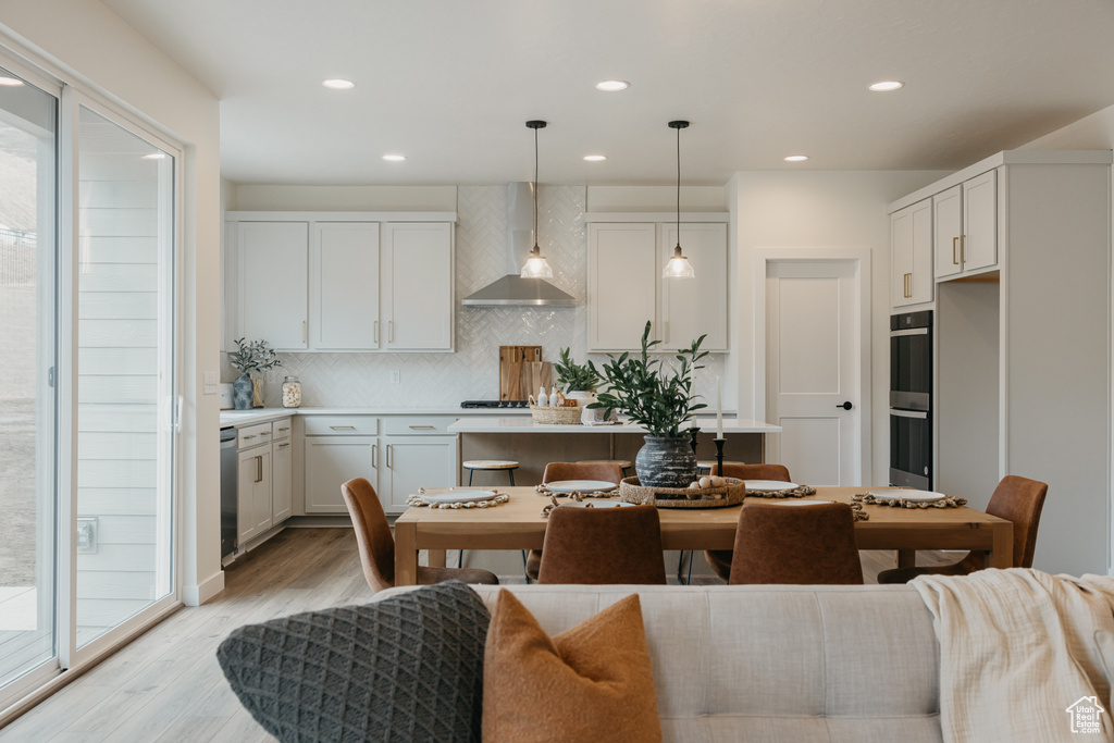 Kitchen featuring wall chimney range hood, light wood-type flooring, backsplash, recessed lighting, and light countertops