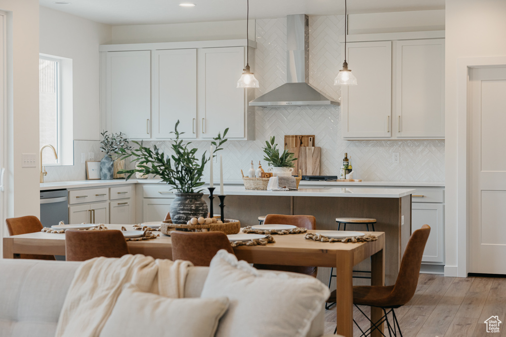 Kitchen with wall chimney exhaust hood, dishwasher, light countertops, decorative backsplash, and light wood finished floors