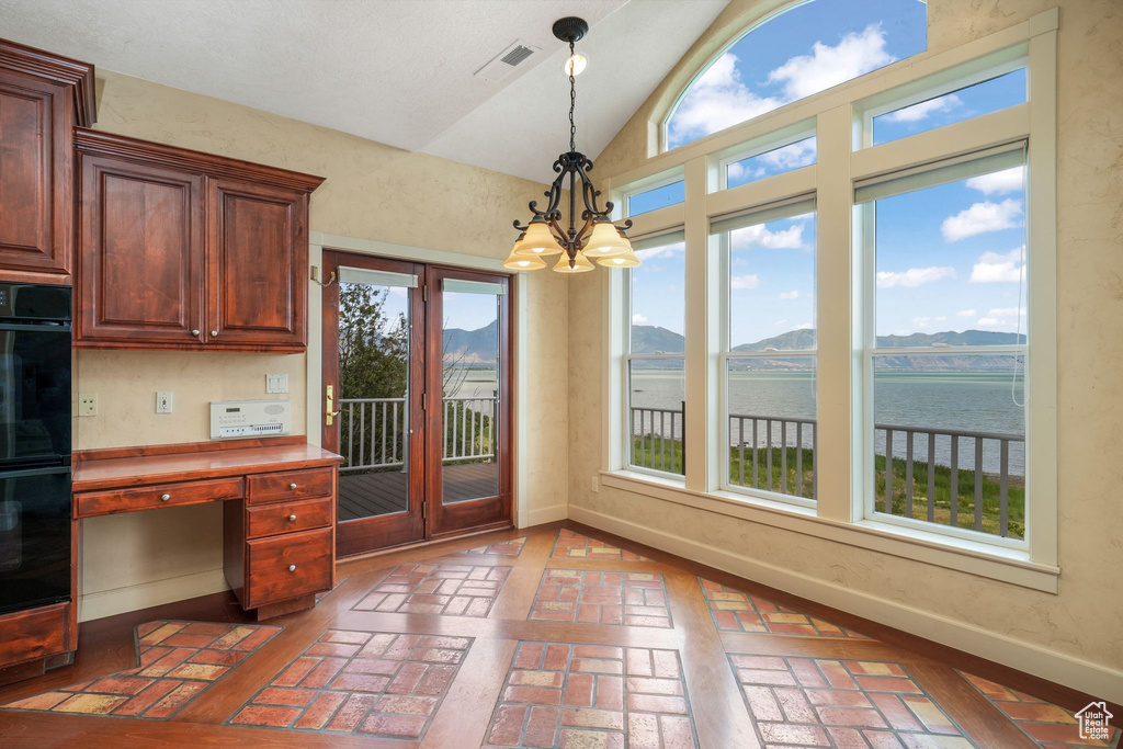 Kitchen featuring brick flooring, vaulted ceiling, a chandelier, hanging light fixtures, and a water and mountain view