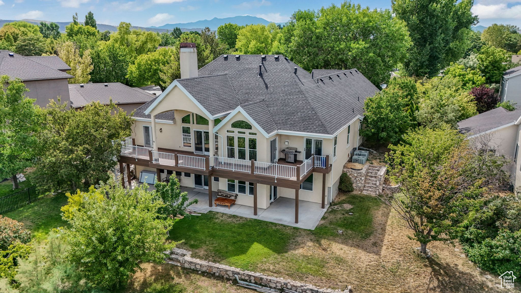 Rear view of house featuring a patio, a chimney, stucco siding, a wooden deck, and a lawn