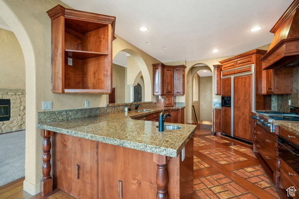 Kitchen featuring paneled built in refrigerator, custom range hood, stainless steel gas stovetop, arched walkways, and recessed lighting