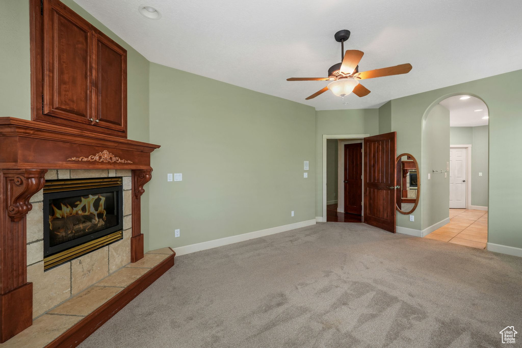 Unfurnished living room featuring a tiled fireplace, ceiling fan, light carpet, arched walkways, and recessed lighting