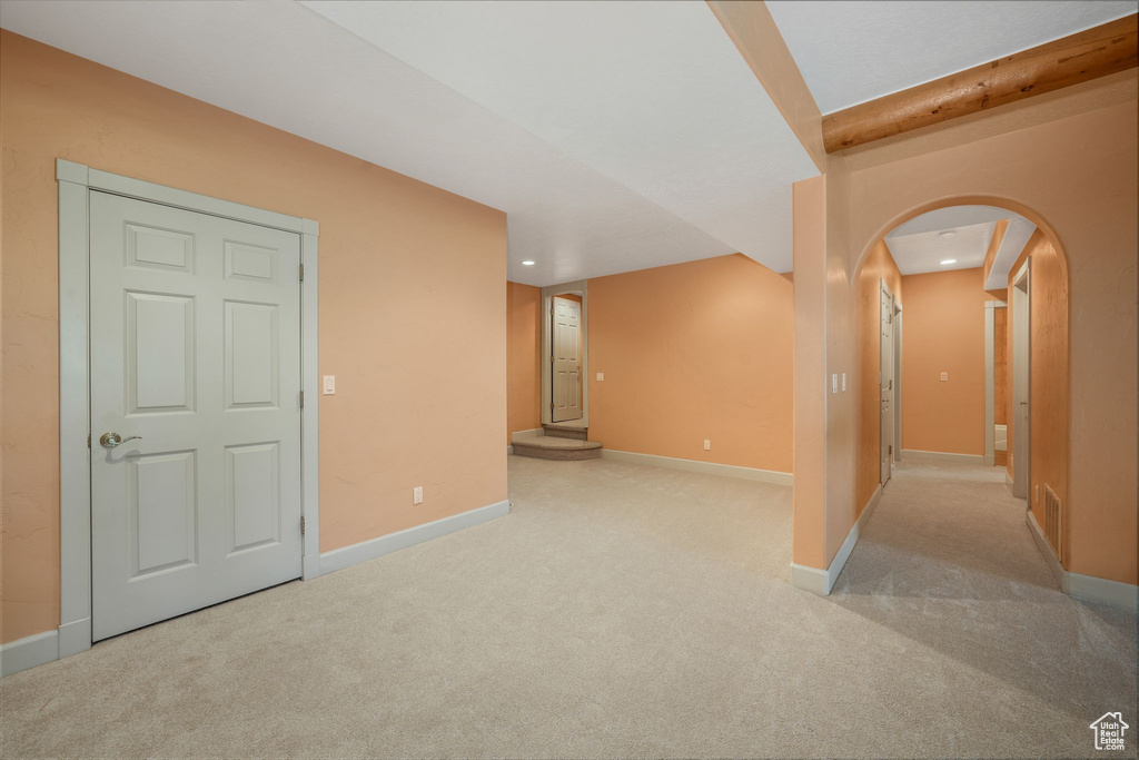 Carpeted empty room featuring arched walkways, recessed lighting, and beamed ceiling