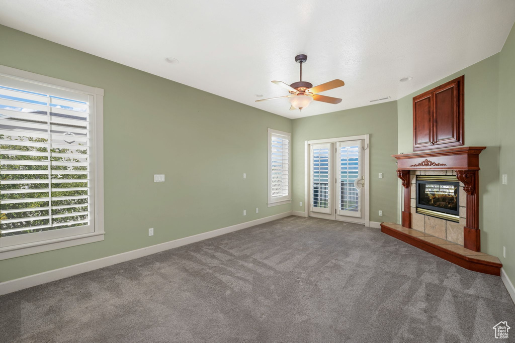 Unfurnished living room featuring a tile fireplace, plenty of natural light, and carpet floors