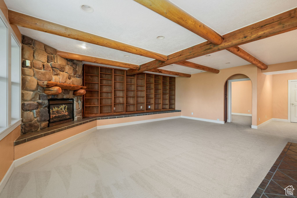 Unfurnished living room featuring beamed ceiling, carpet floors, a stone fireplace, arched walkways, and recessed lighting