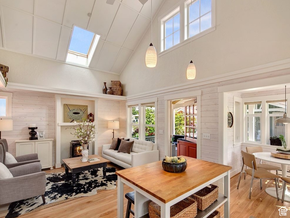 Dining space with a skylight, high vaulted ceiling, light wood-style floors, wood walls, and healthy amount of natural light