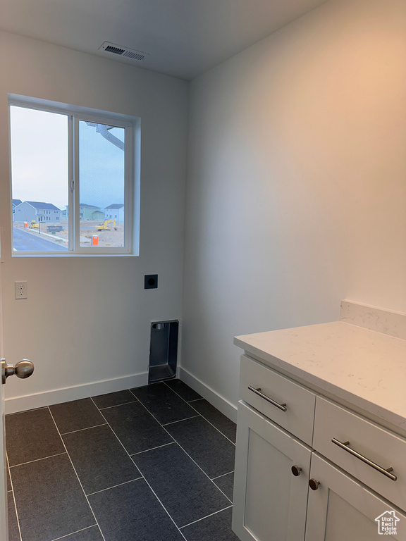 Washroom featuring hookup for an electric dryer, dark tile patterned flooring, and cabinet space