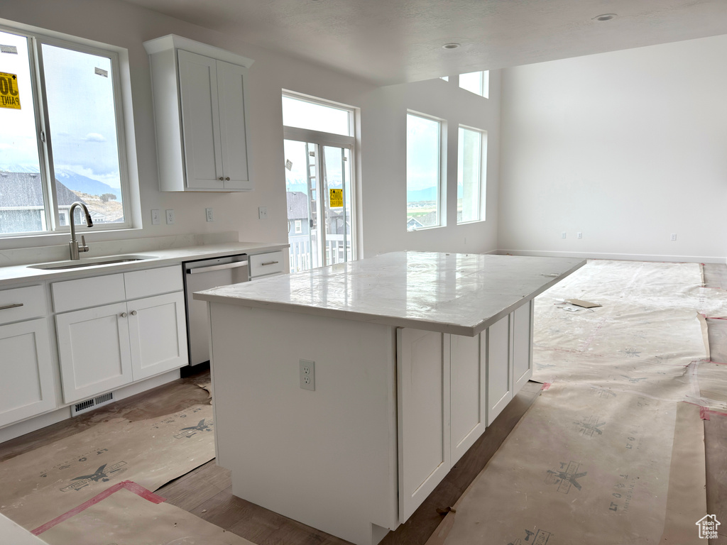 Kitchen featuring stainless steel dishwasher, a center island, white cabinetry, and light wood-style flooring