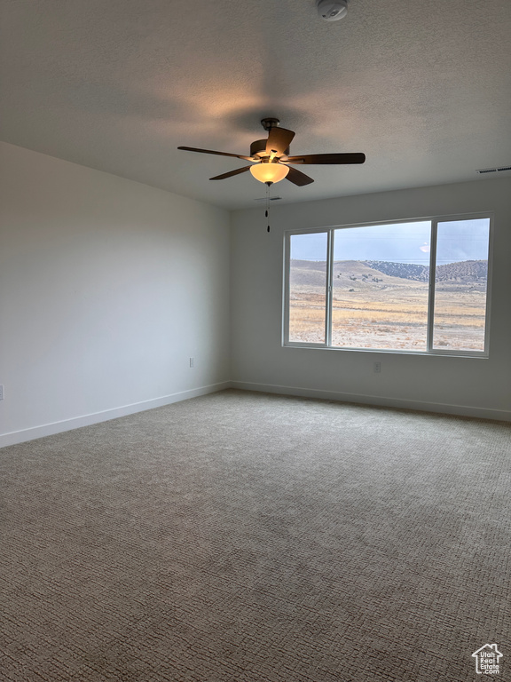 Carpeted spare room featuring ceiling fan, a textured ceiling, and a smoke detector
