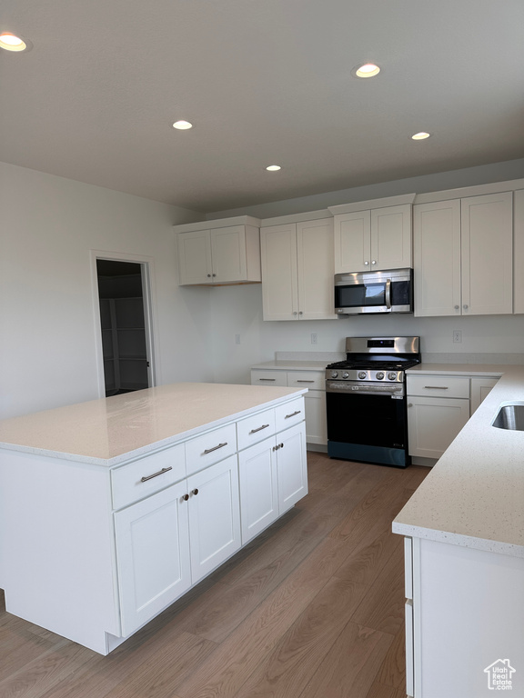 Kitchen with stainless steel appliances, light wood-style floors, recessed lighting, white cabinets, and light stone countertops