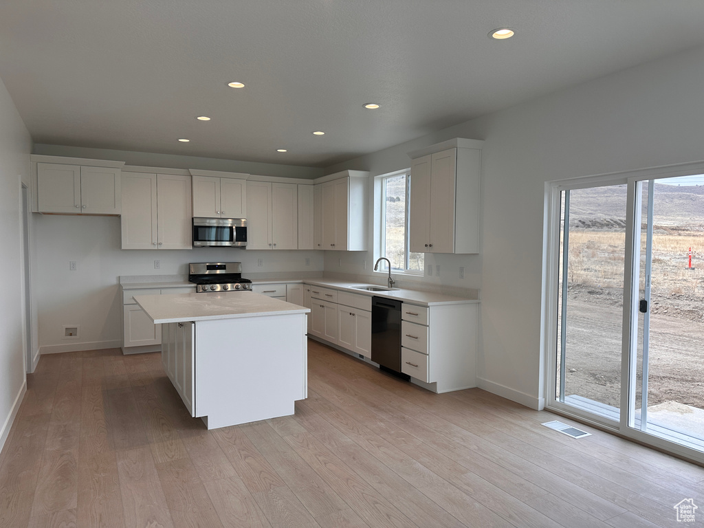 Kitchen with appliances with stainless steel finishes, recessed lighting, light wood-type flooring, light countertops, and a kitchen island