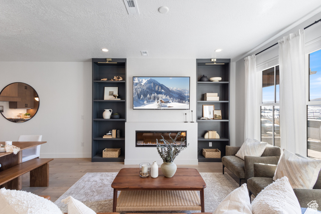 Living room with a glass covered fireplace, built in features, light wood finished floors, and a textured ceiling