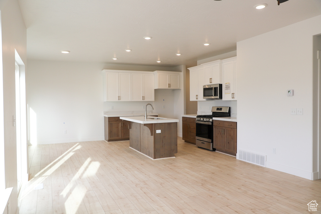 Kitchen with stainless steel appliances, white cabinets, light countertops, light wood-style floors, and recessed lighting